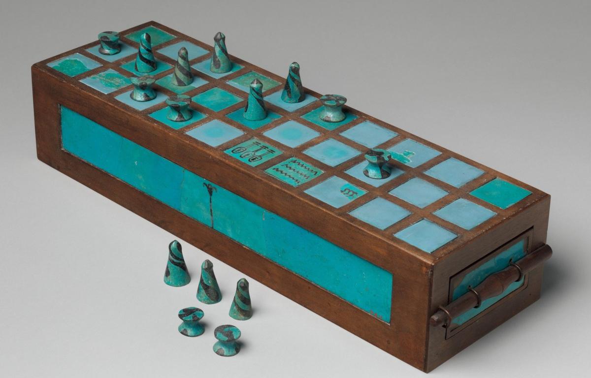 Photo of a blue Senet board from the Met Museum, with pieces laid out on and in front of the board.